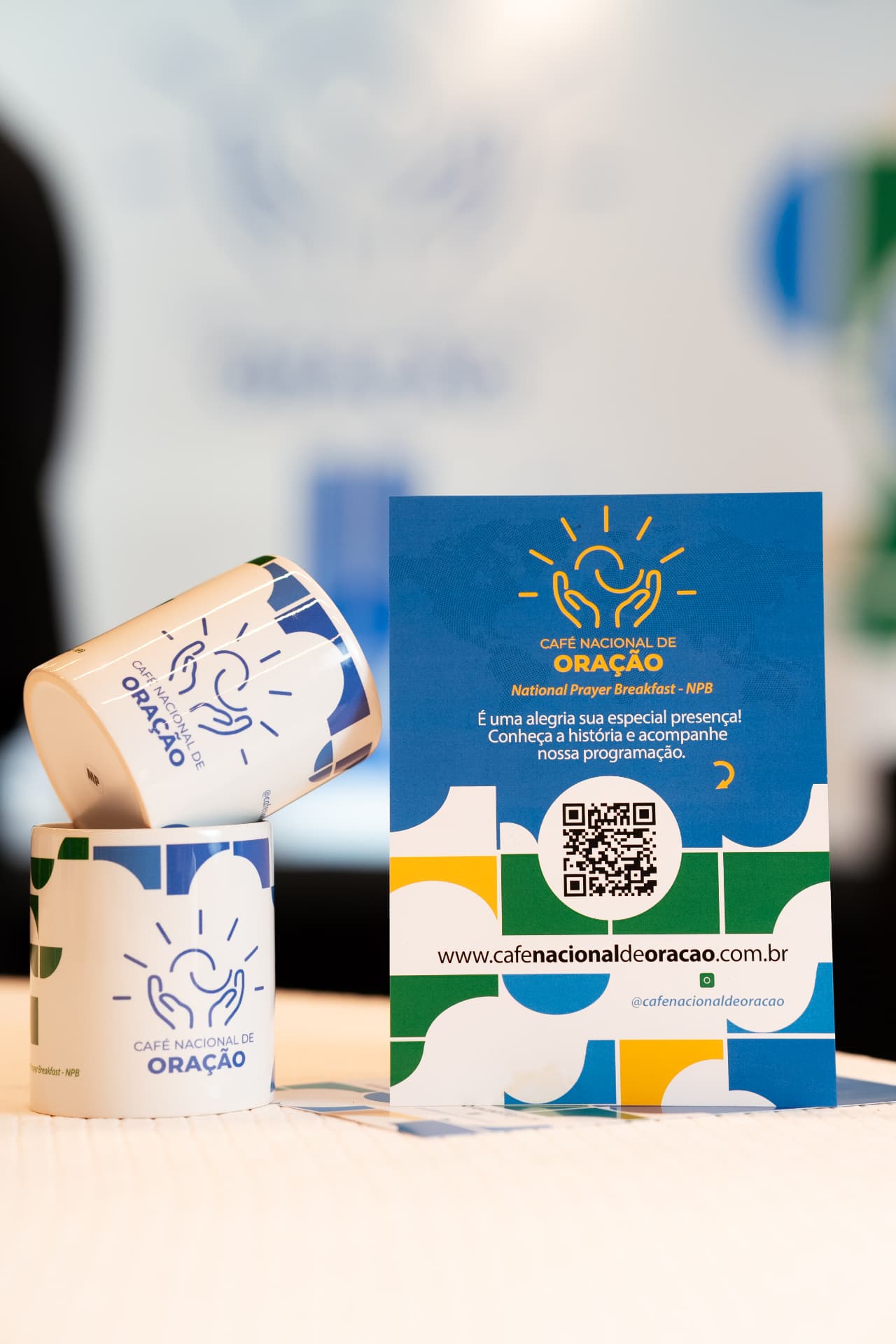 Canecas e convite do Café Nacional de Oração sobre a mesa